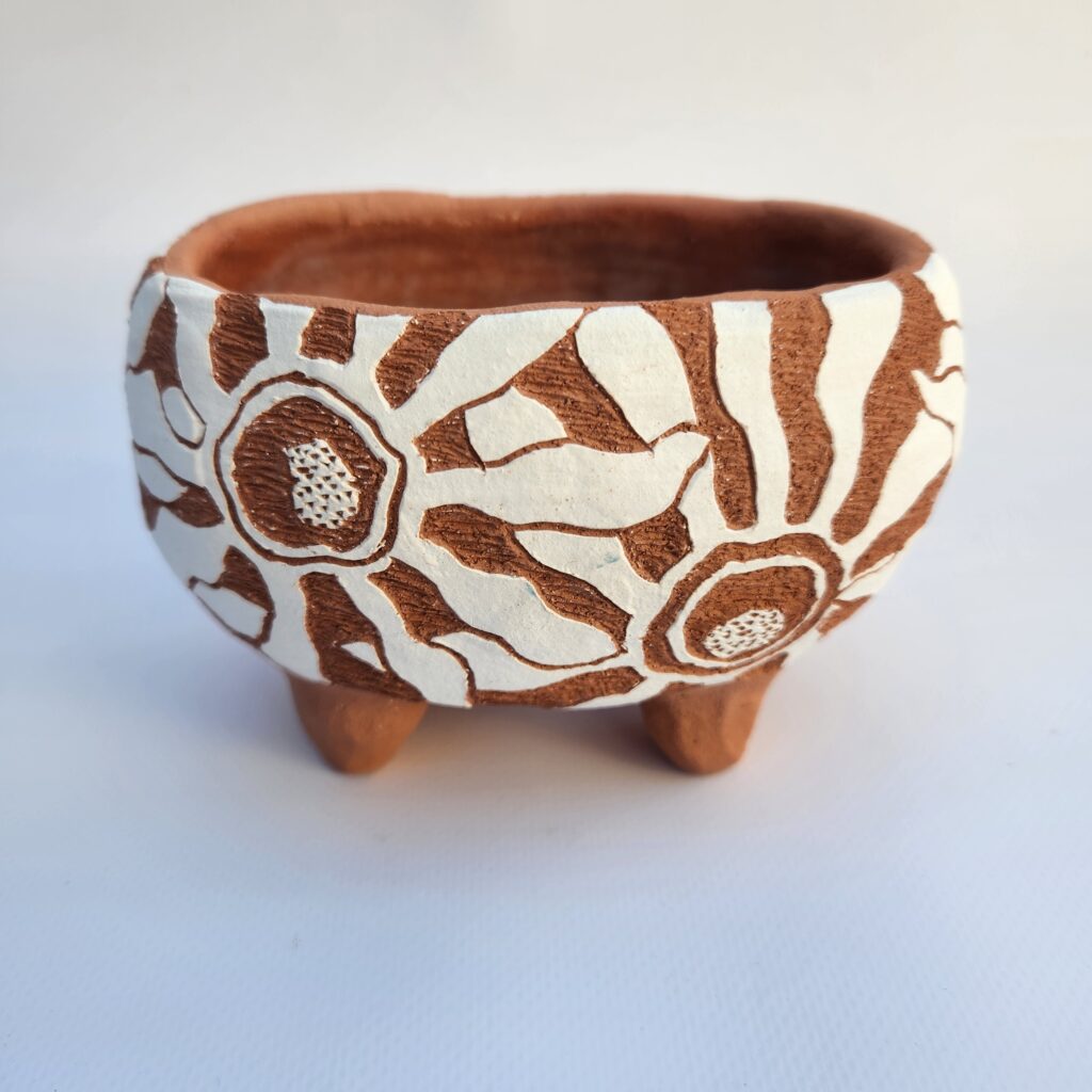 A decorative clay pot with a brown and white sgraffito design hand-built.